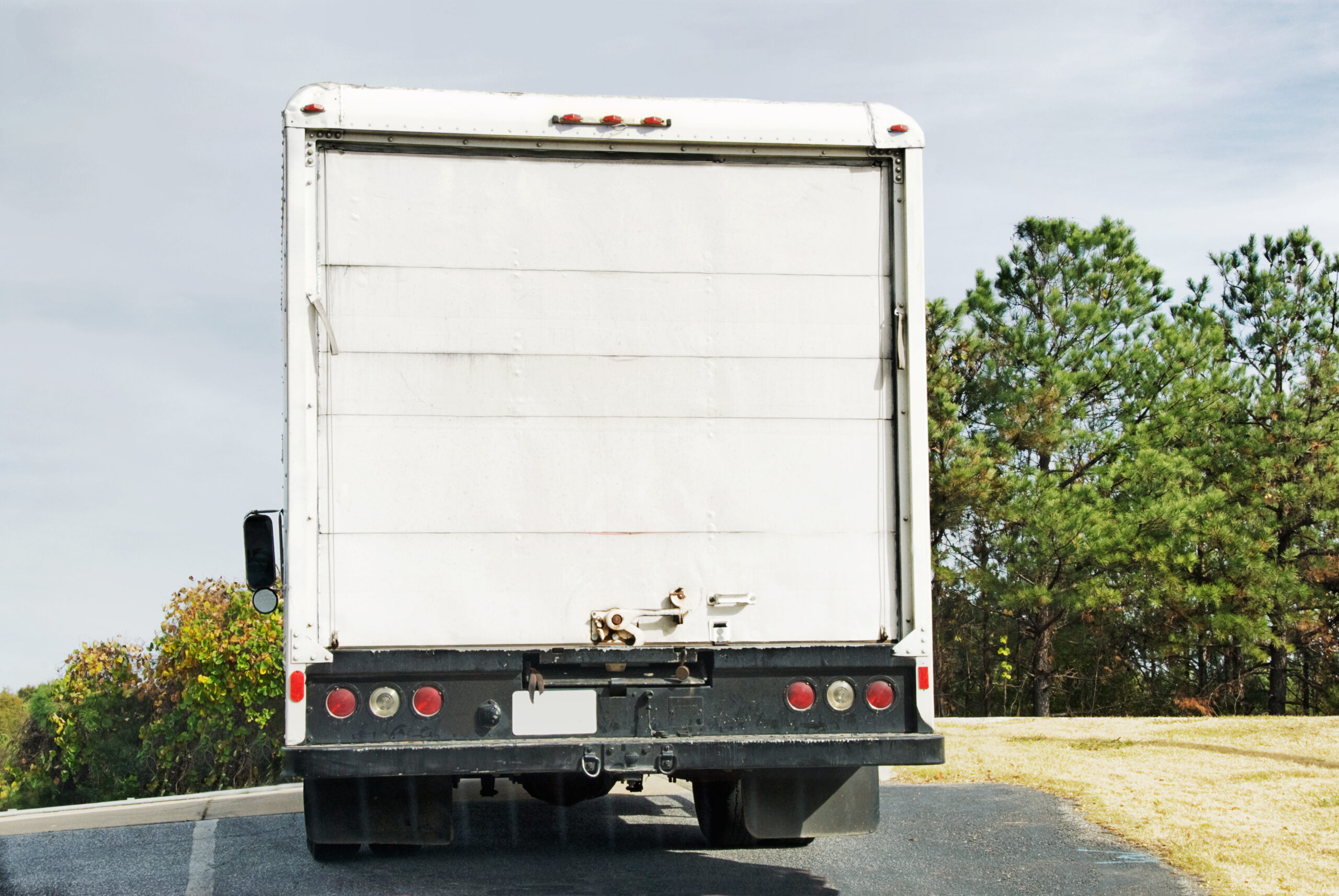 The back side of a commercial white delivery truck with a blank door moving down the highway.